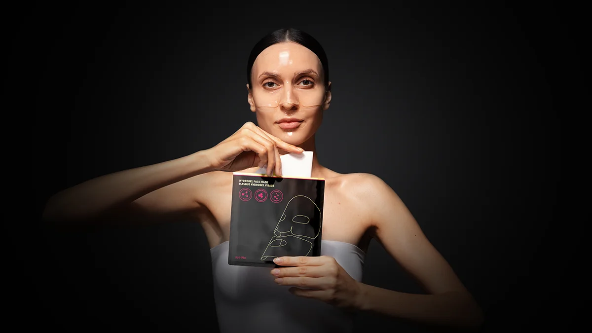 A woman pulling FAQ Collagen mask for glass skin out of a sachet ona a dark background